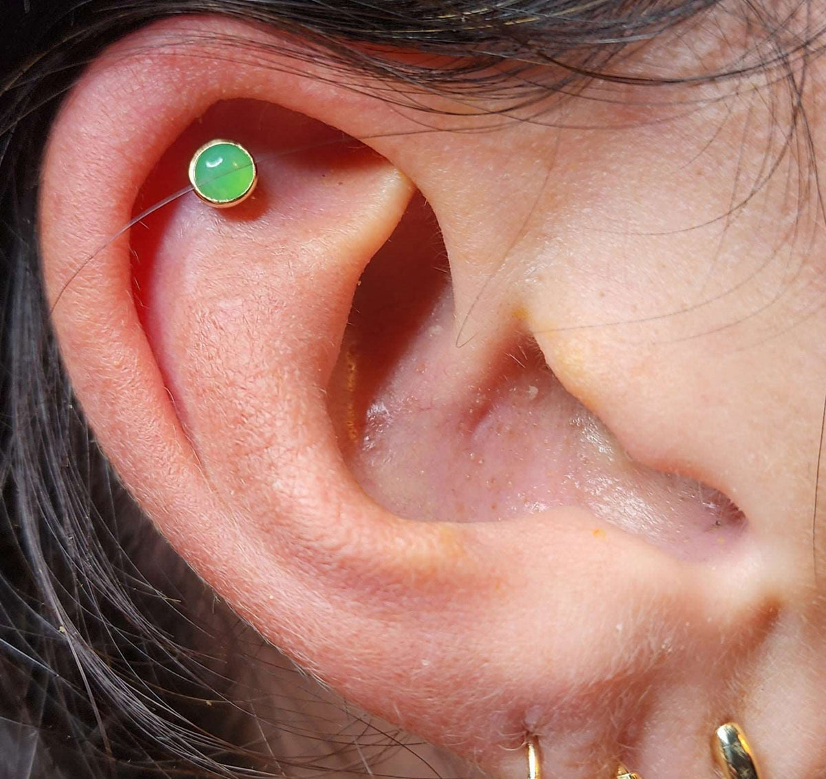 Green cabochon jewelry worn in an upper-ear piercing