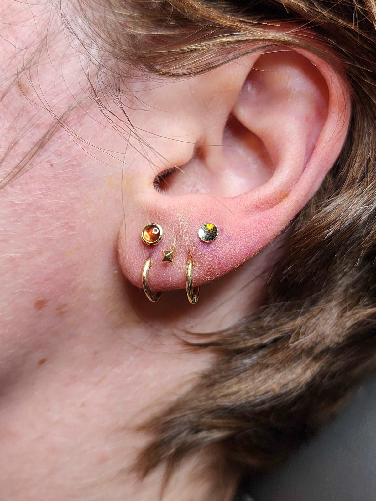 Gold rings and coloured gemstone studs in a curated ear