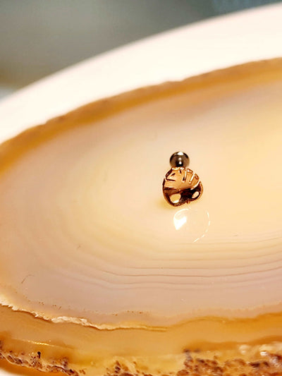 Rose gold monstera leaf-shaped jewelry end on a pale stone display