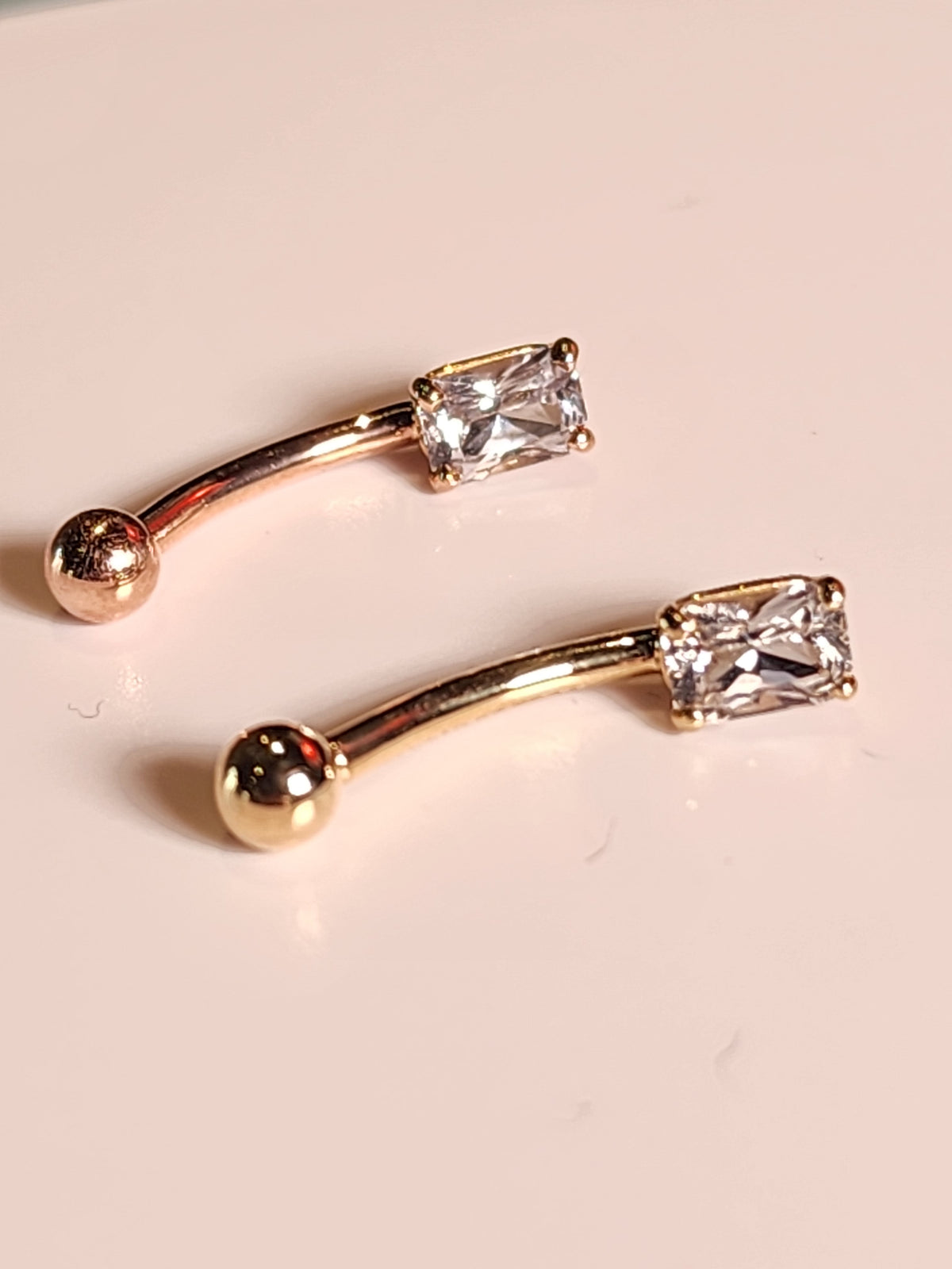 Yellow and rose gold curved navel barbells with white sapphire ends