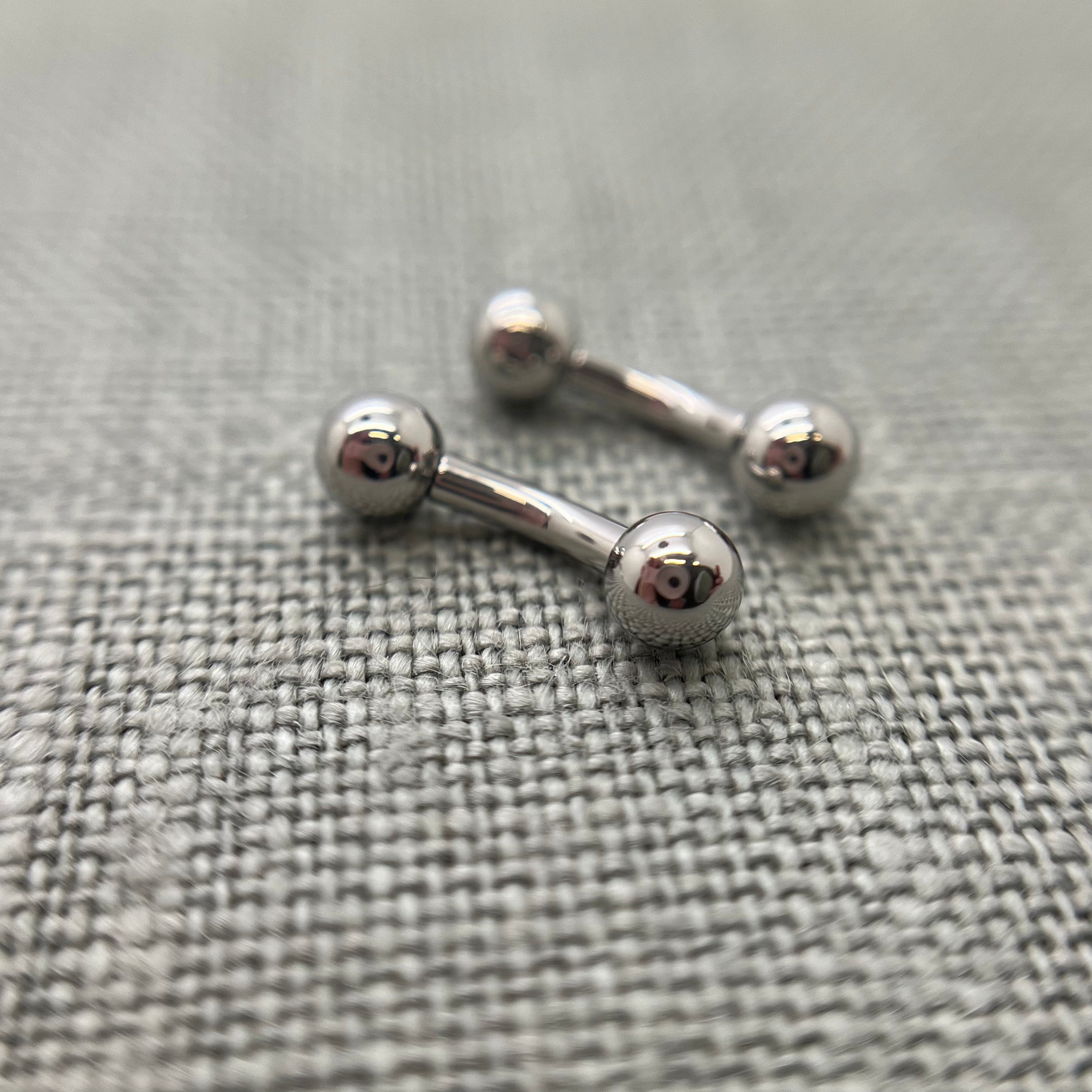 Polished stainless steel curved barbells on grey fabric