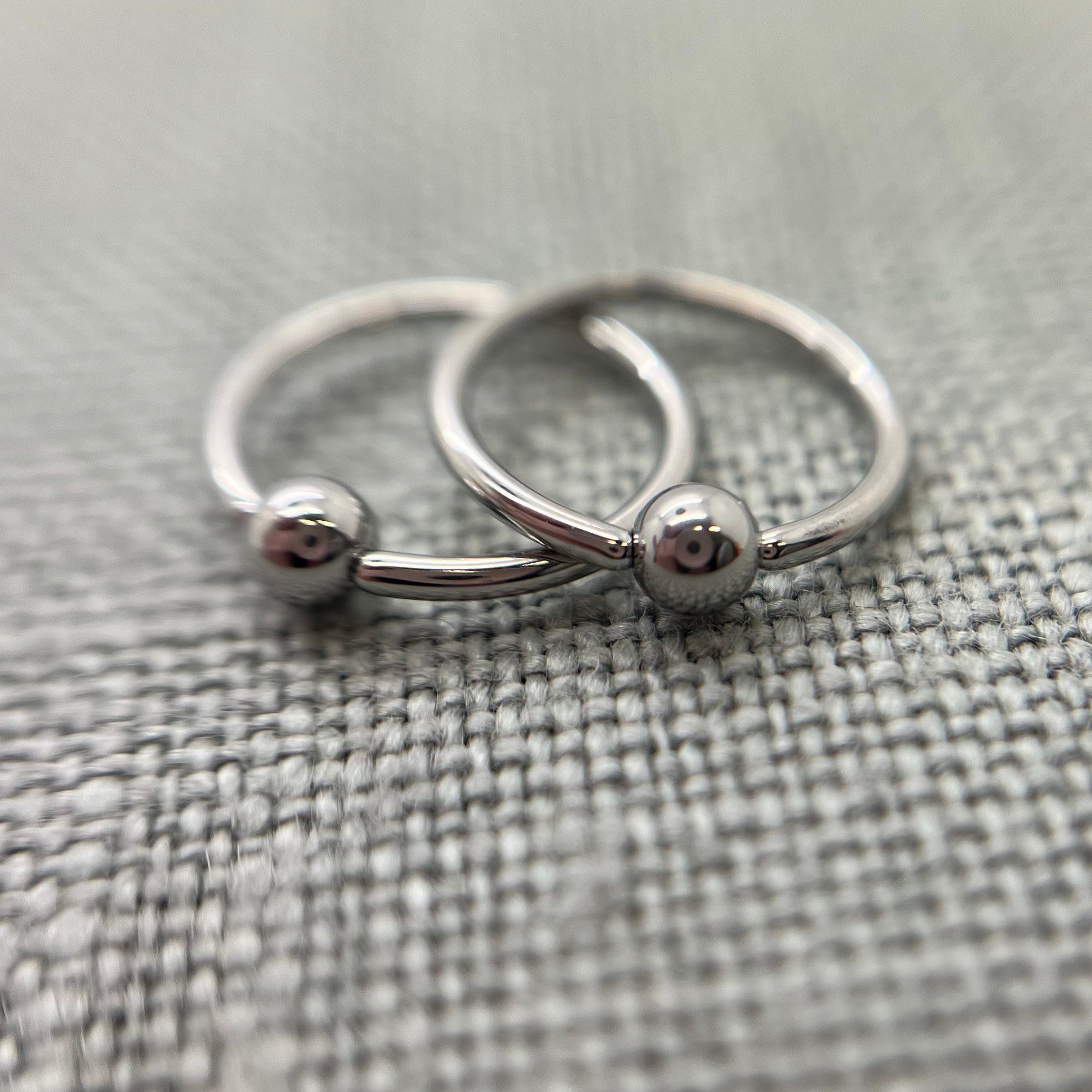 Two polished stainless steel captive bead rings on grey fabric