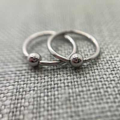 Two polished stainless steel captive bead rings on grey fabric