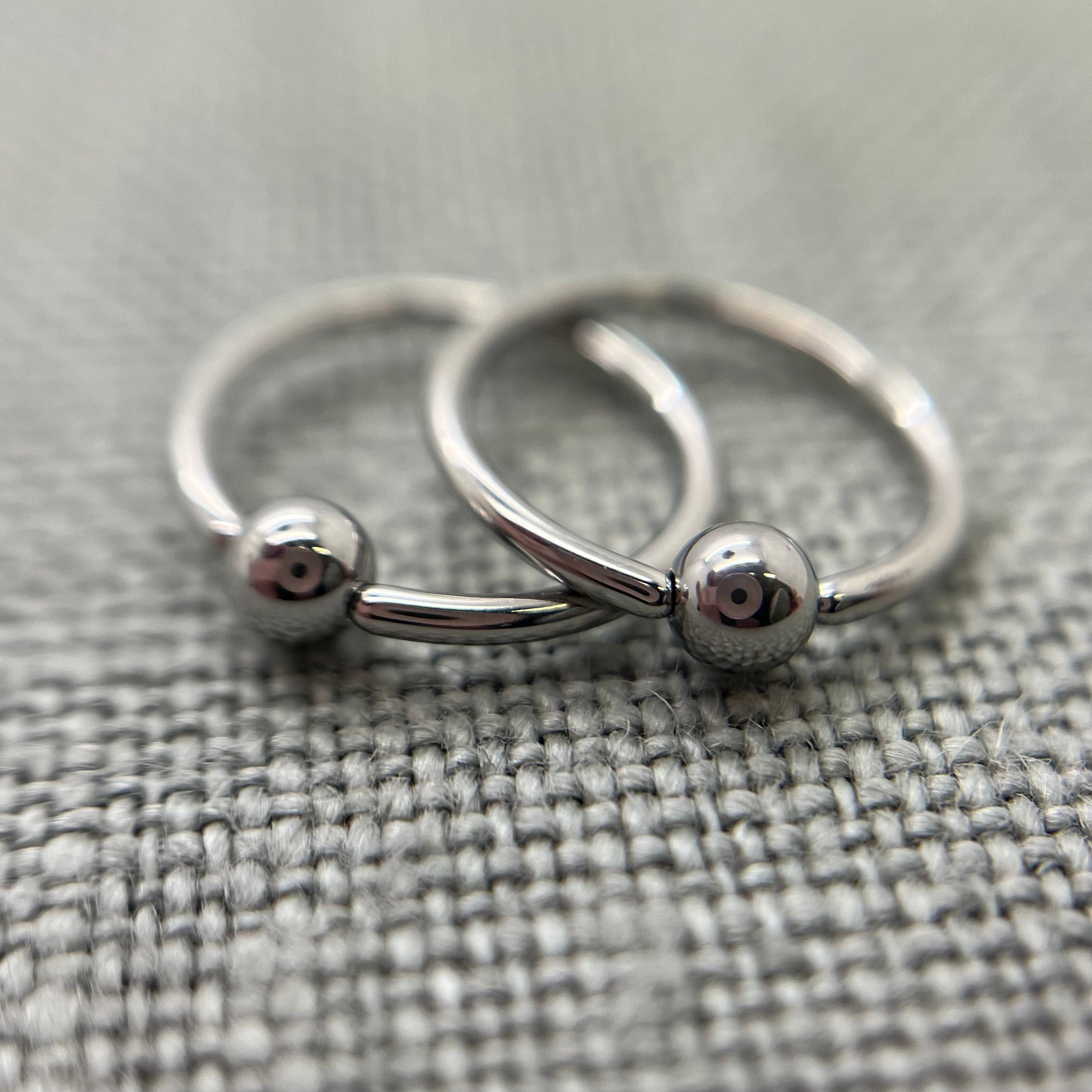 Two polished stainless steel captive bead rings on grey fabric