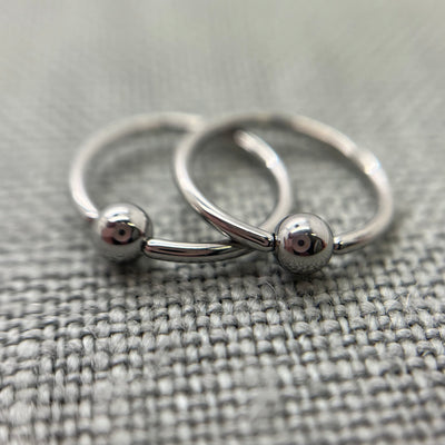 Two polished stainless steel captive bead rings on grey fabric