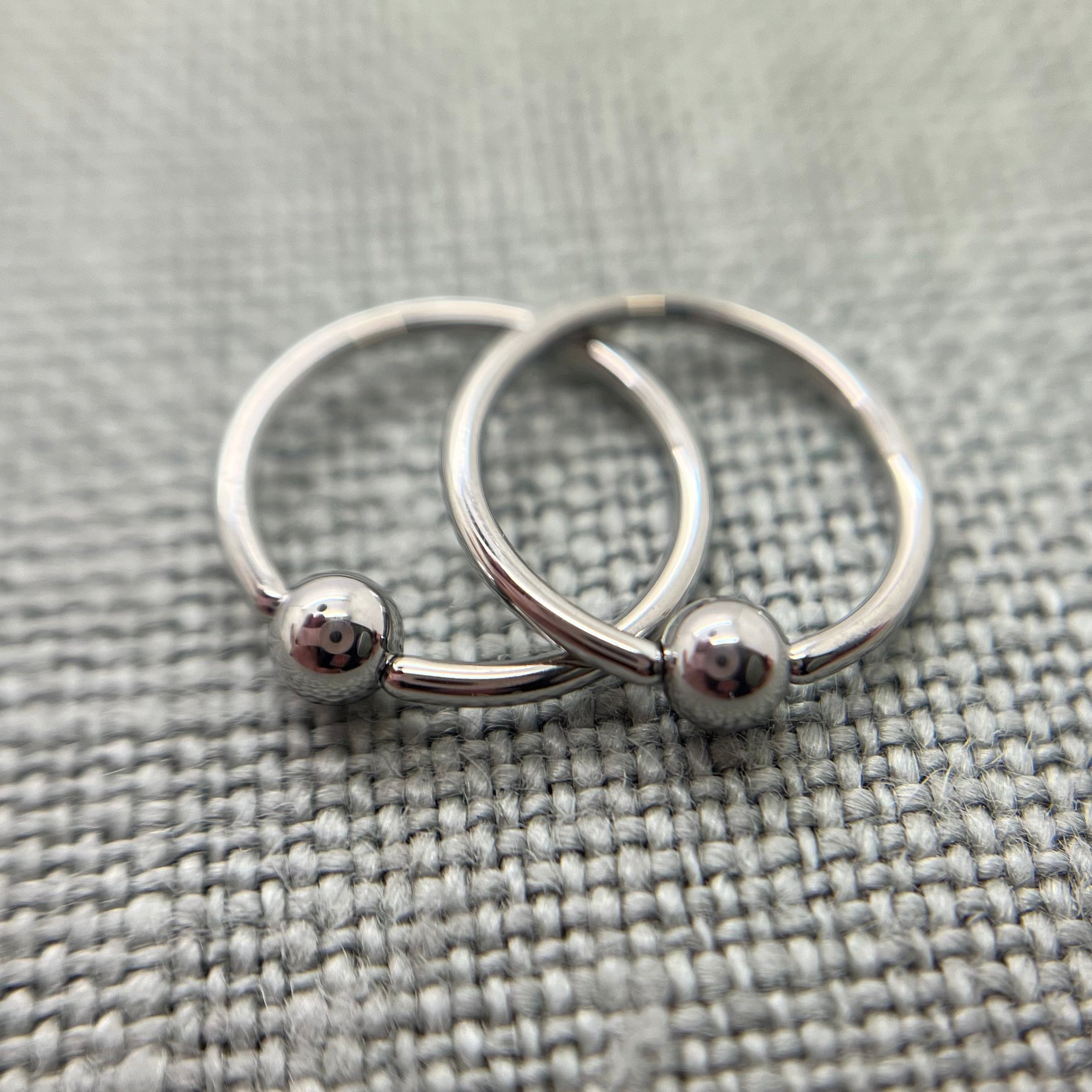 Two polished stainless steel captive bead rings on grey fabric