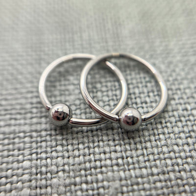 Two polished stainless steel captive bead rings on grey fabric