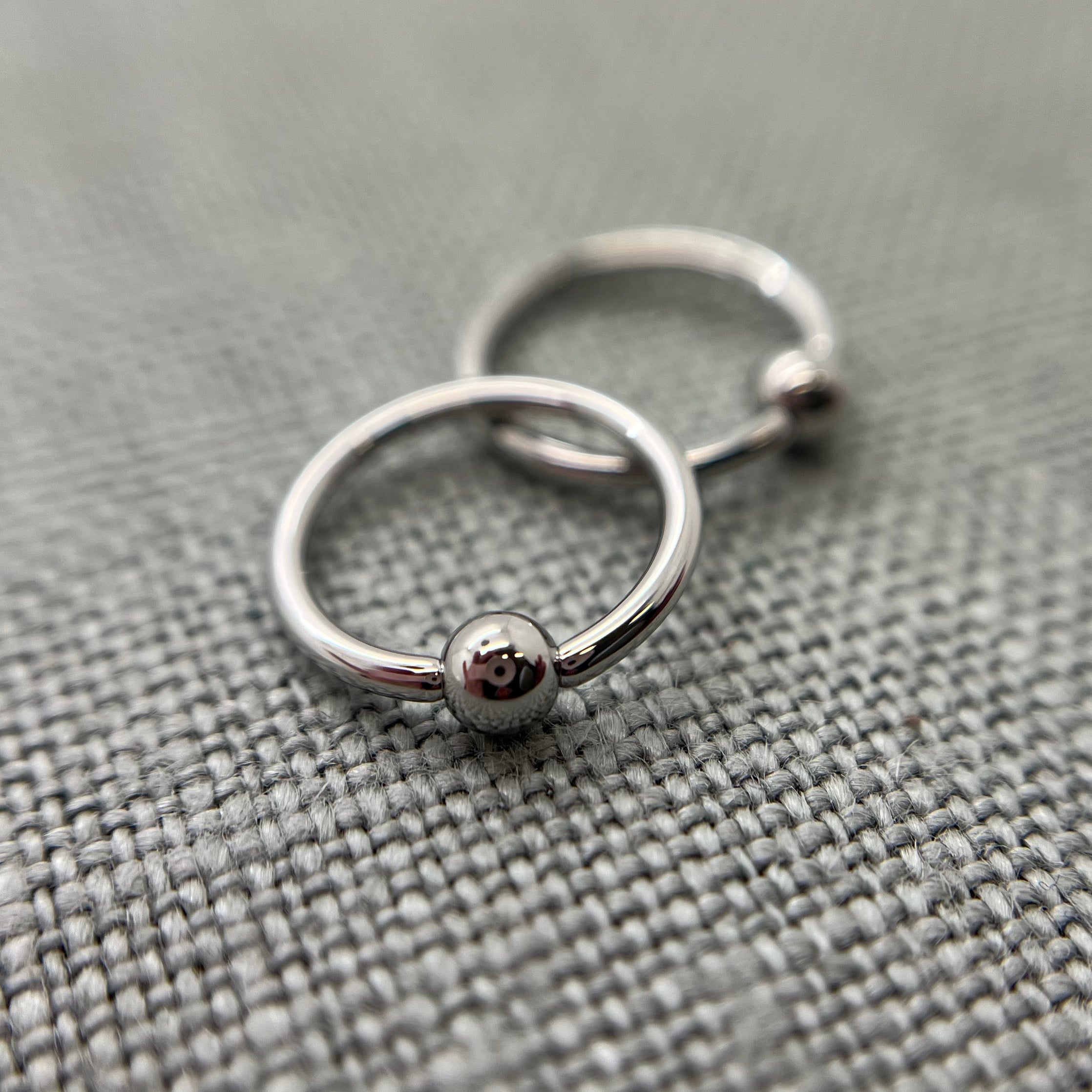 Two polished stainless steel captive bead rings on grey fabric