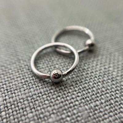Two polished stainless steel captive bead rings on grey fabric