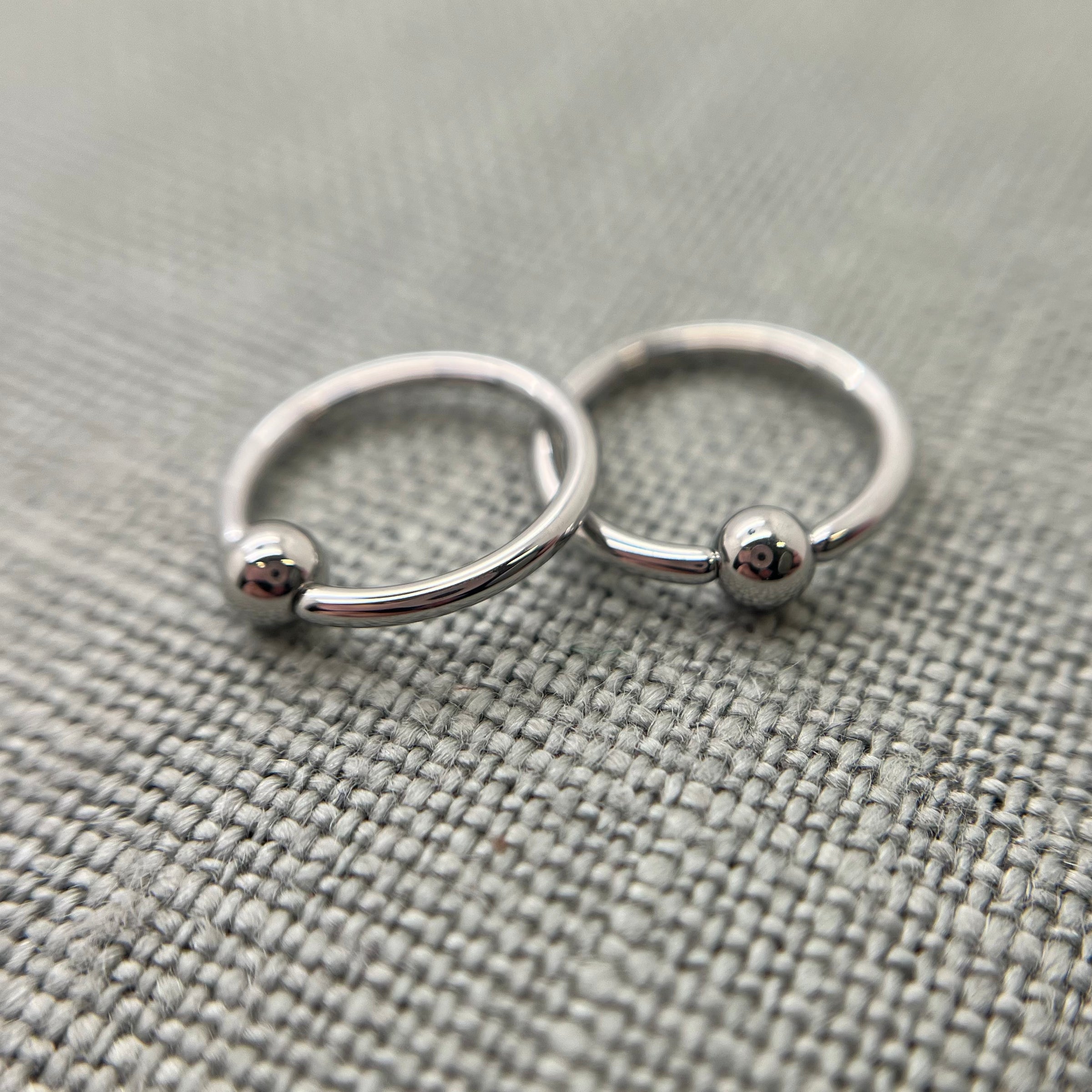 Two polished stainless steel captive bead rings on grey fabric
