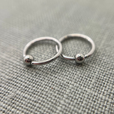 Two polished stainless steel captive bead rings on grey fabric