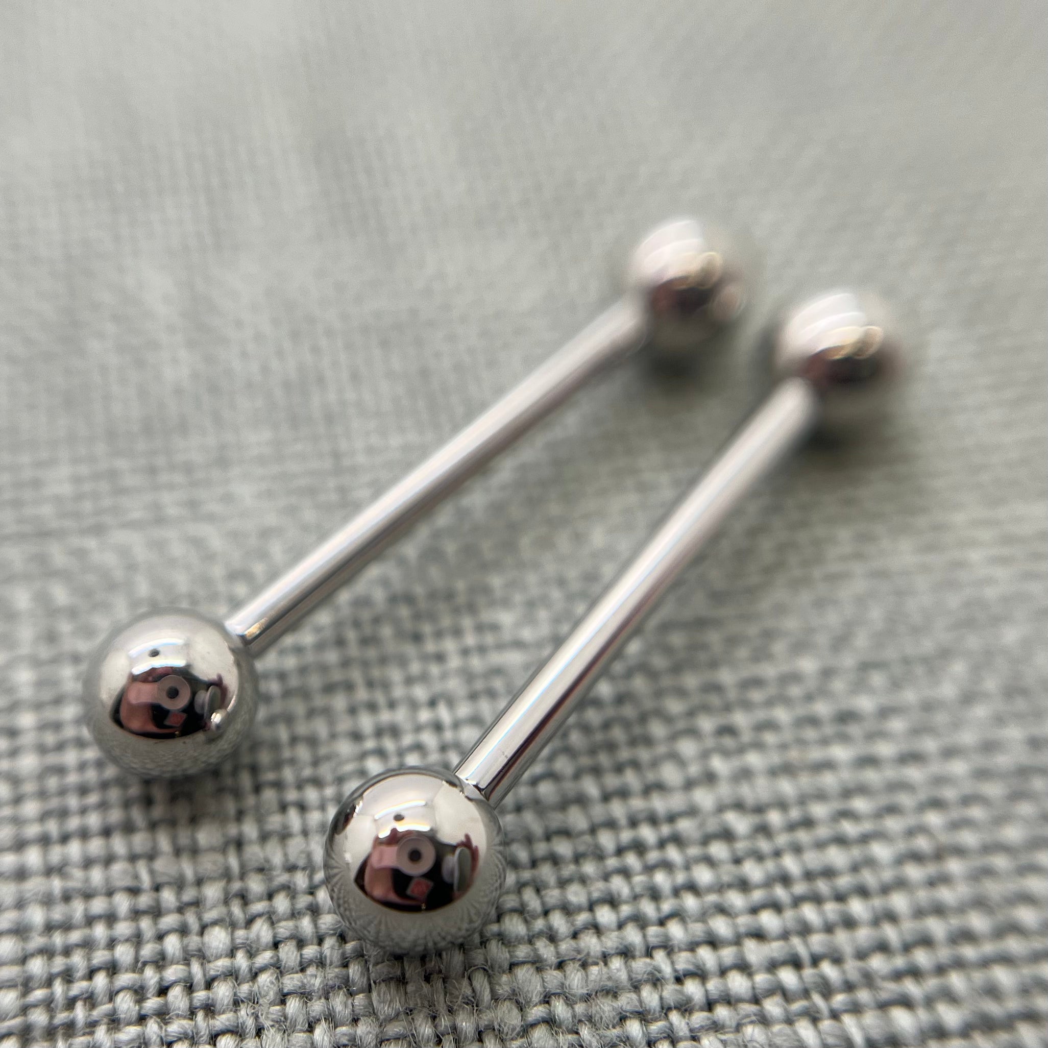 Two polished stainless steel straight barbells on grey fabric