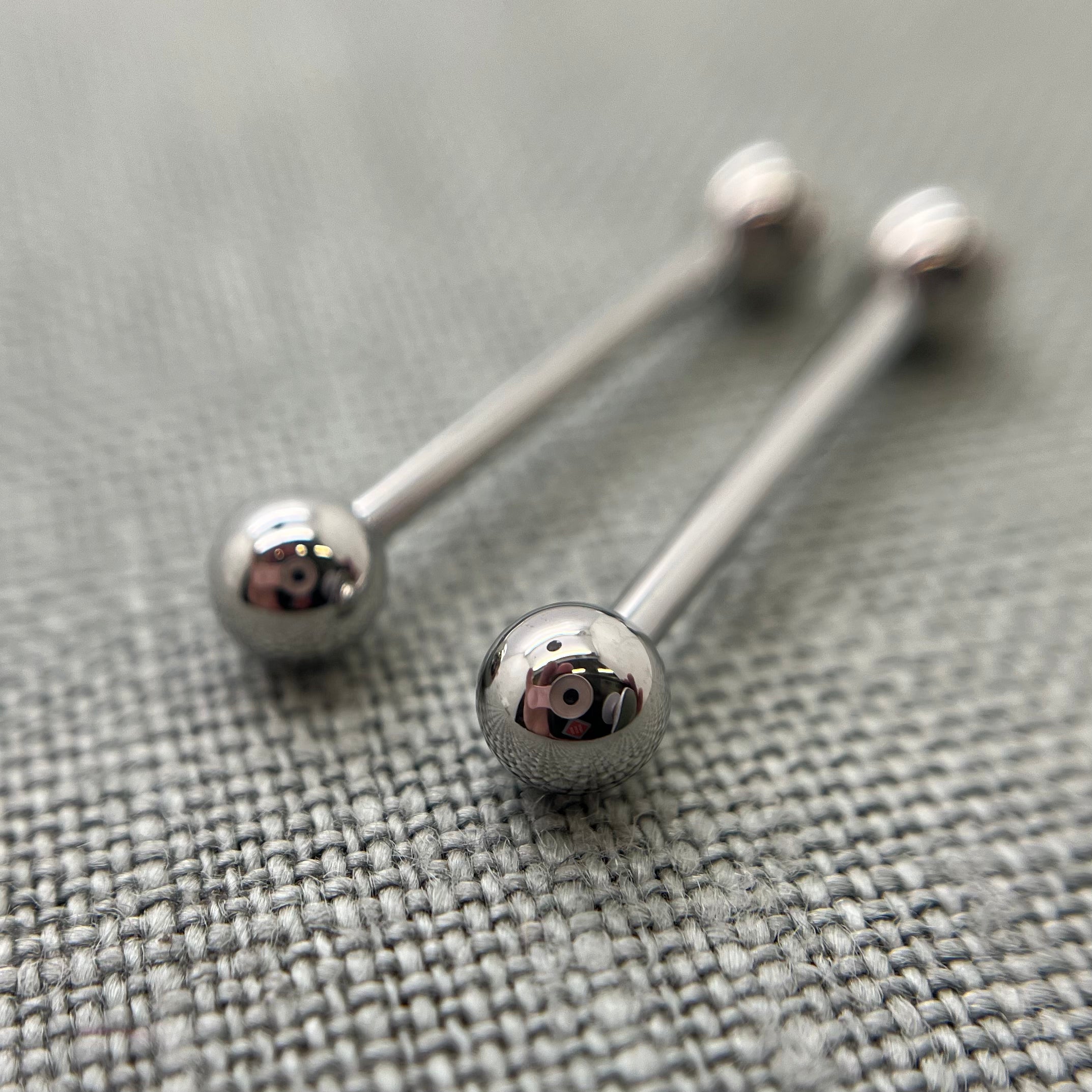 Two polished stainless steel straight barbells on grey fabric