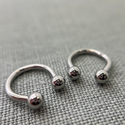Two polished stainless steel circular barbells on grey fabric