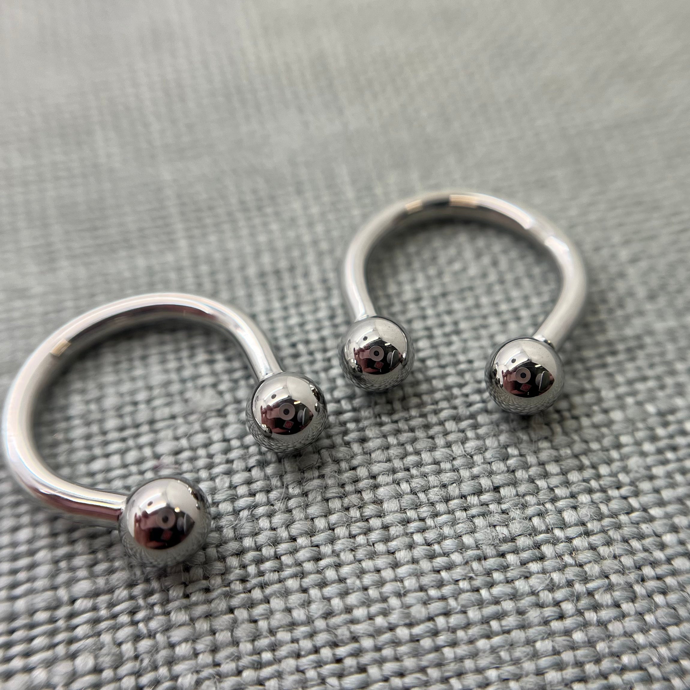 Two polished stainless steel circular barbells on grey fabric