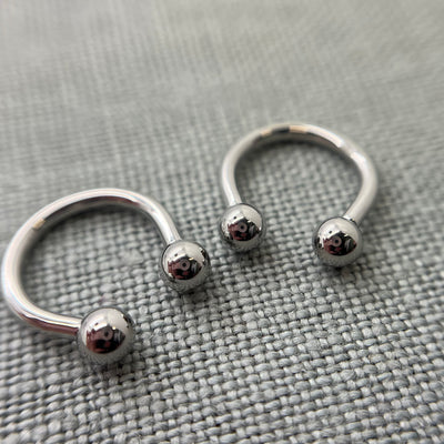 Two polished stainless steel circular barbells on grey fabric