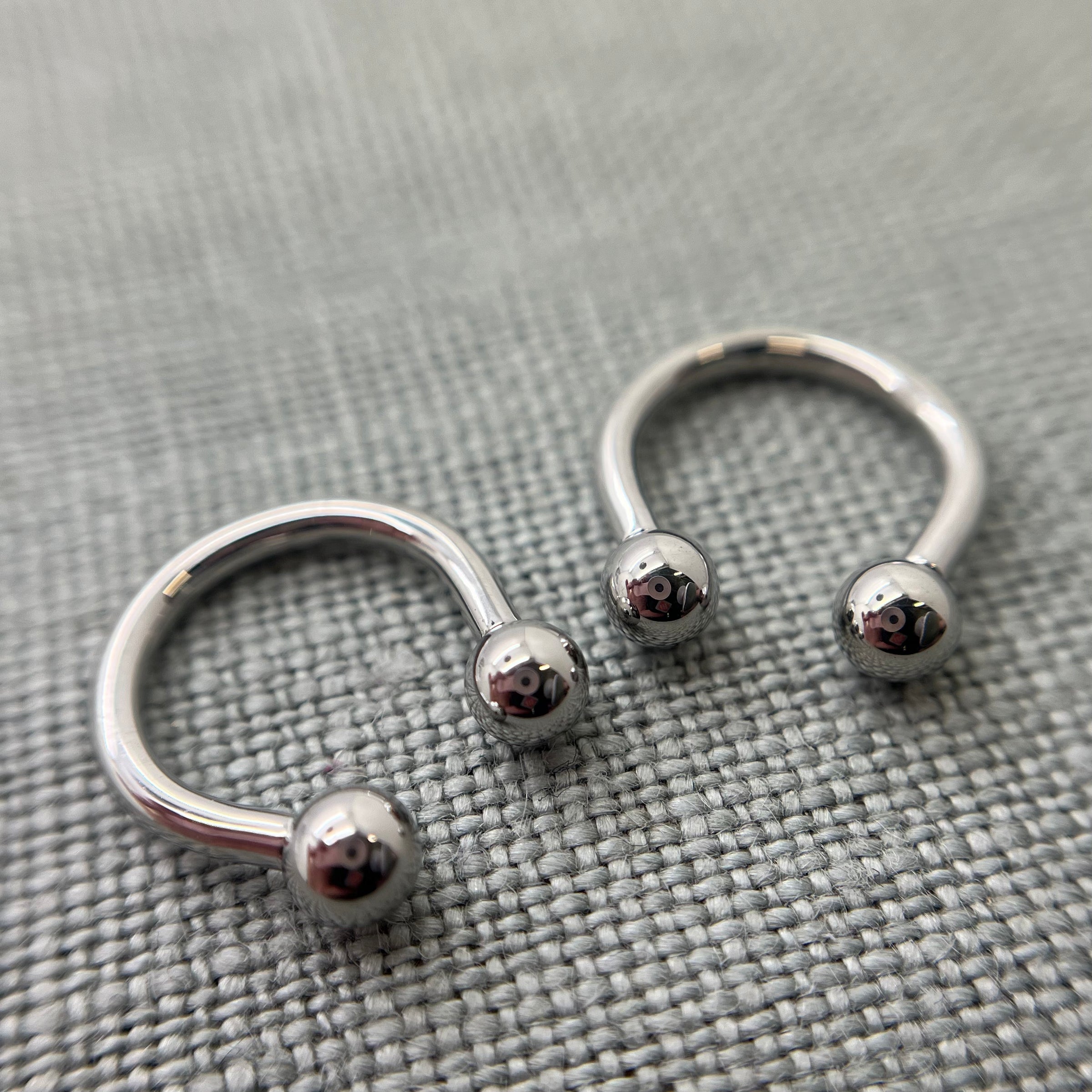 Two polished stainless steel circular barbells on grey fabric