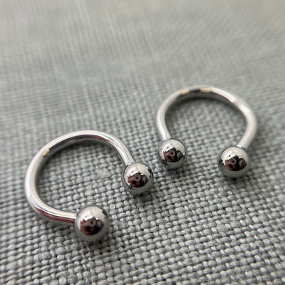 Two polished stainless steel circular barbells on grey fabric