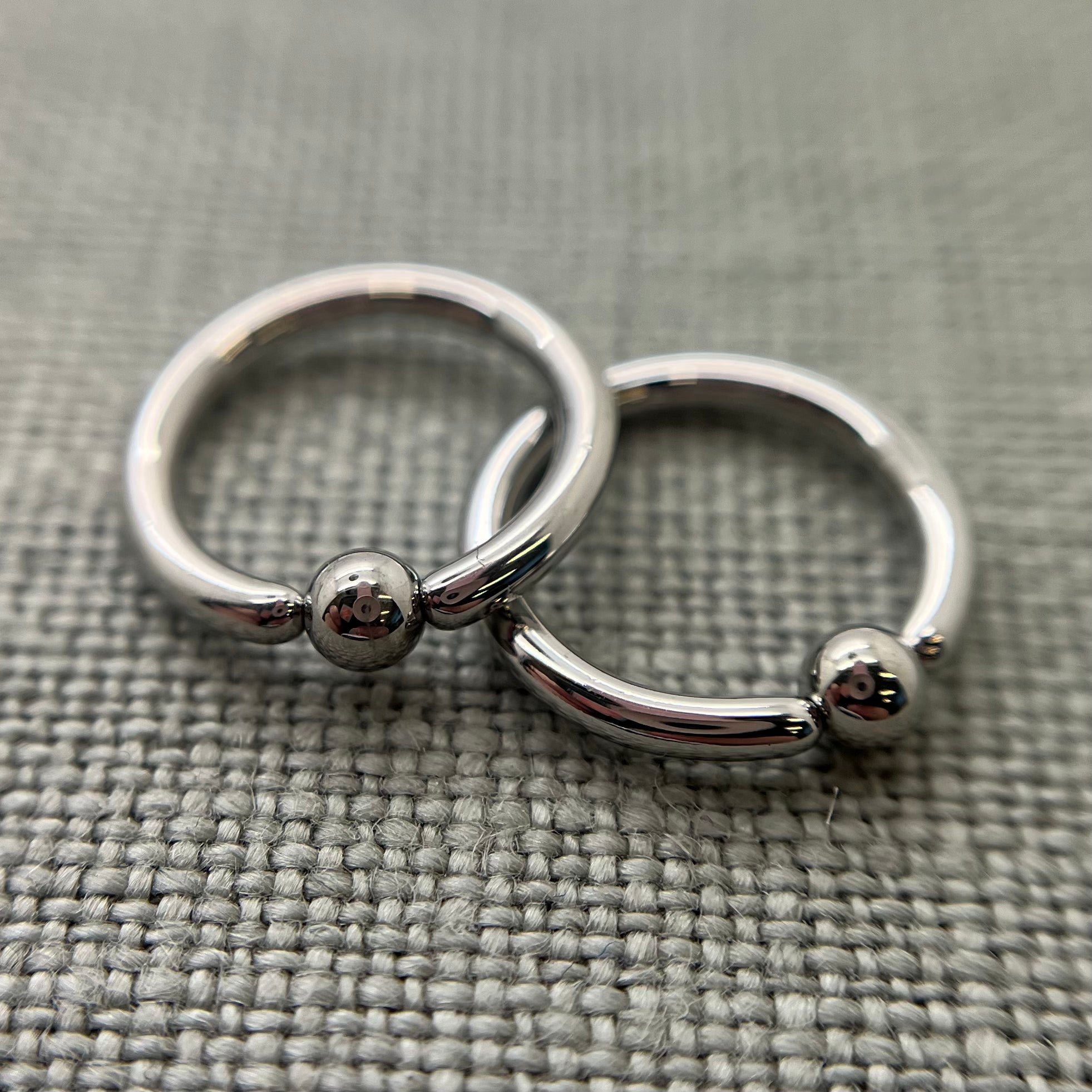 Two polished stainless steel captive bead rings on grey fabric