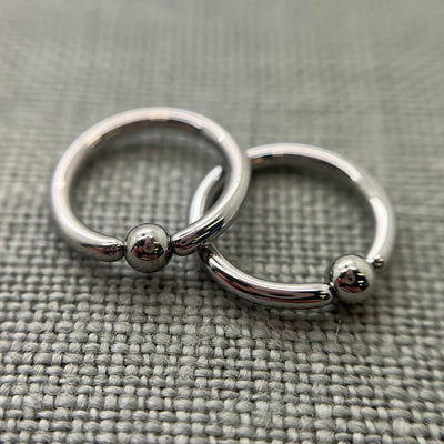 Two polished stainless steel captive bead rings on grey fabric