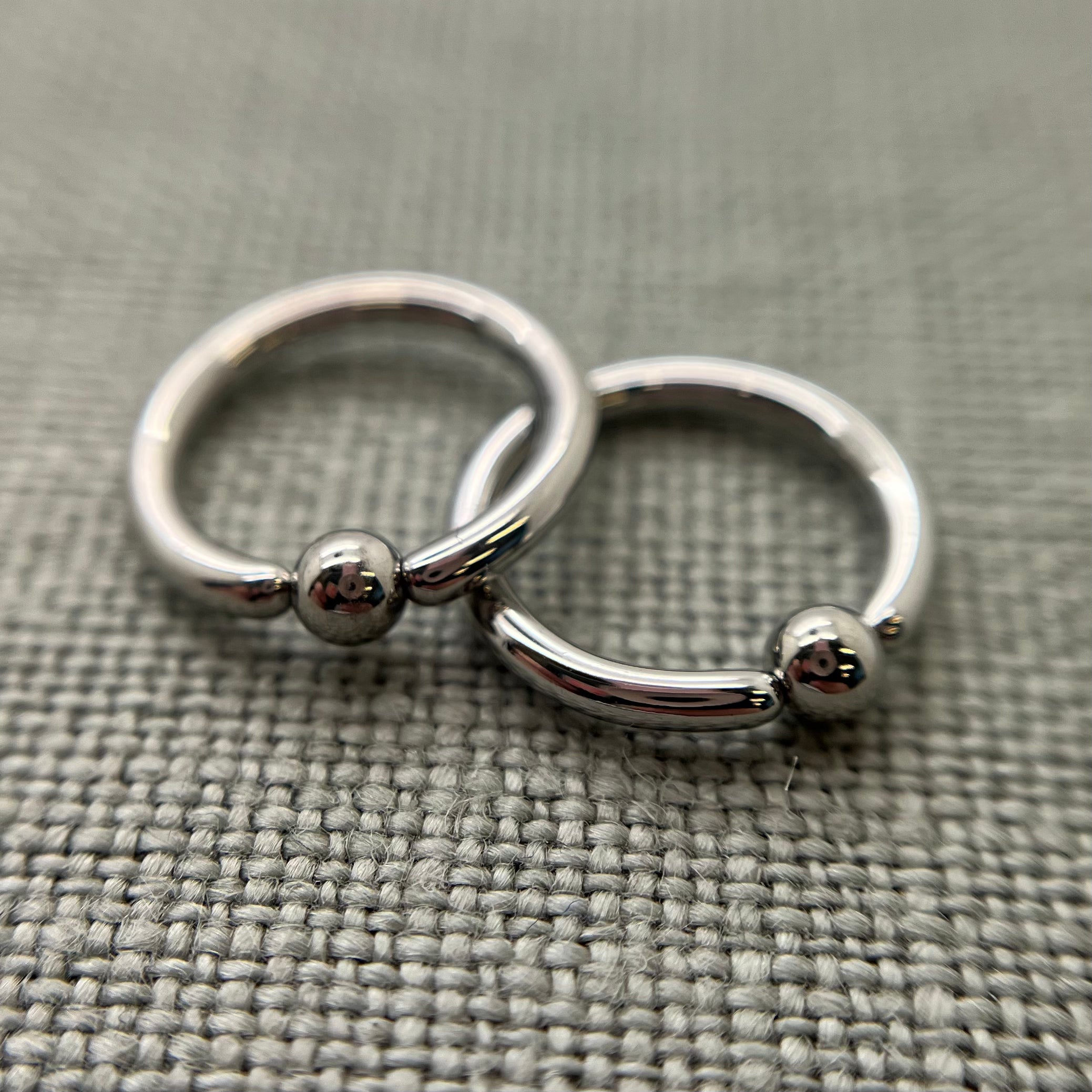 Two polished stainless steel captive bead rings on grey fabric