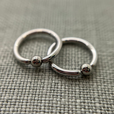 Two polished stainless steel captive bead rings on grey fabric