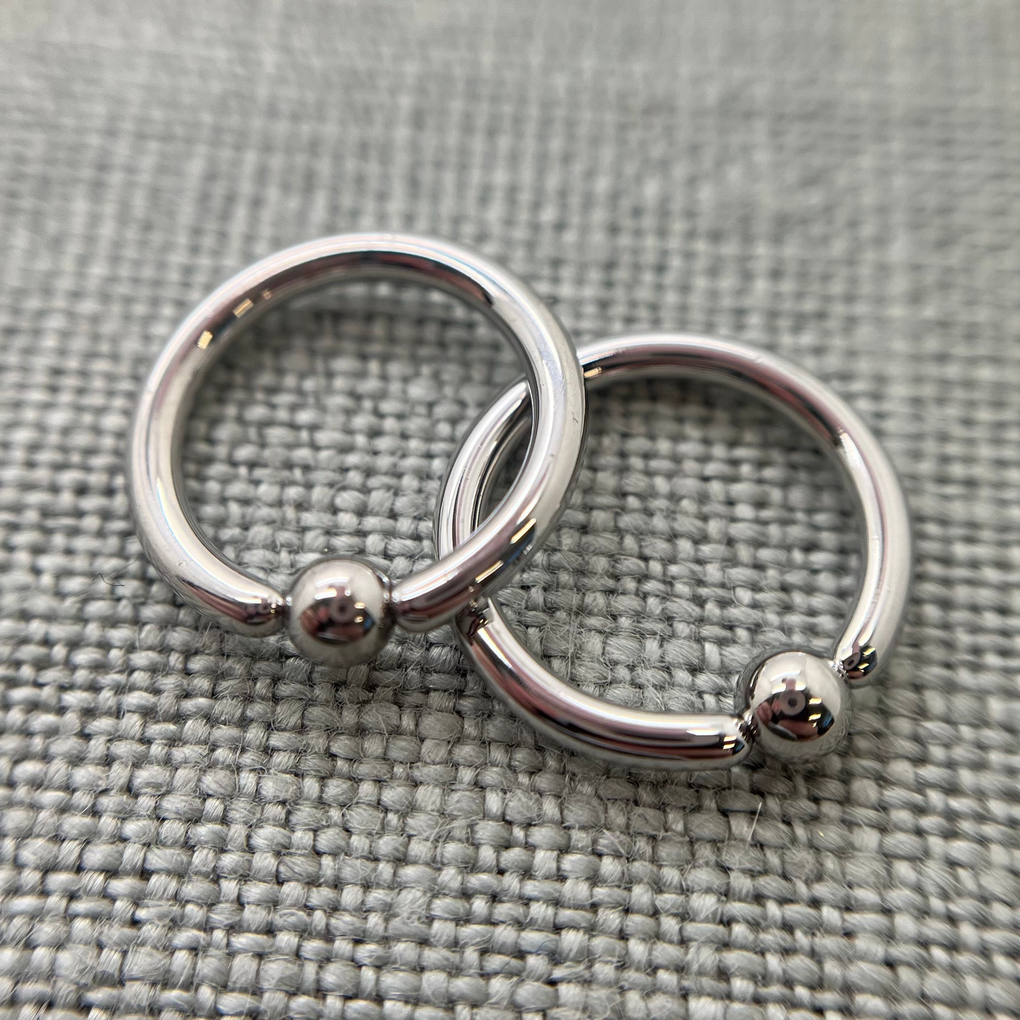 Two polished stainless steel captive bead rings on grey fabric