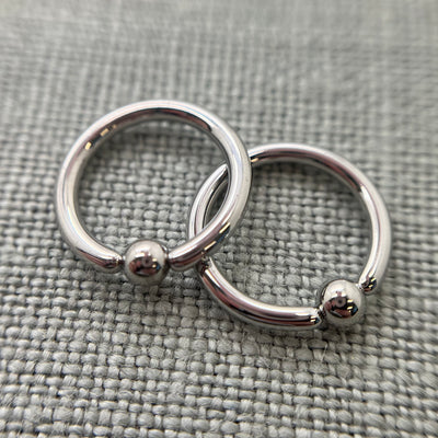 Two polished stainless steel captive bead rings on grey fabric