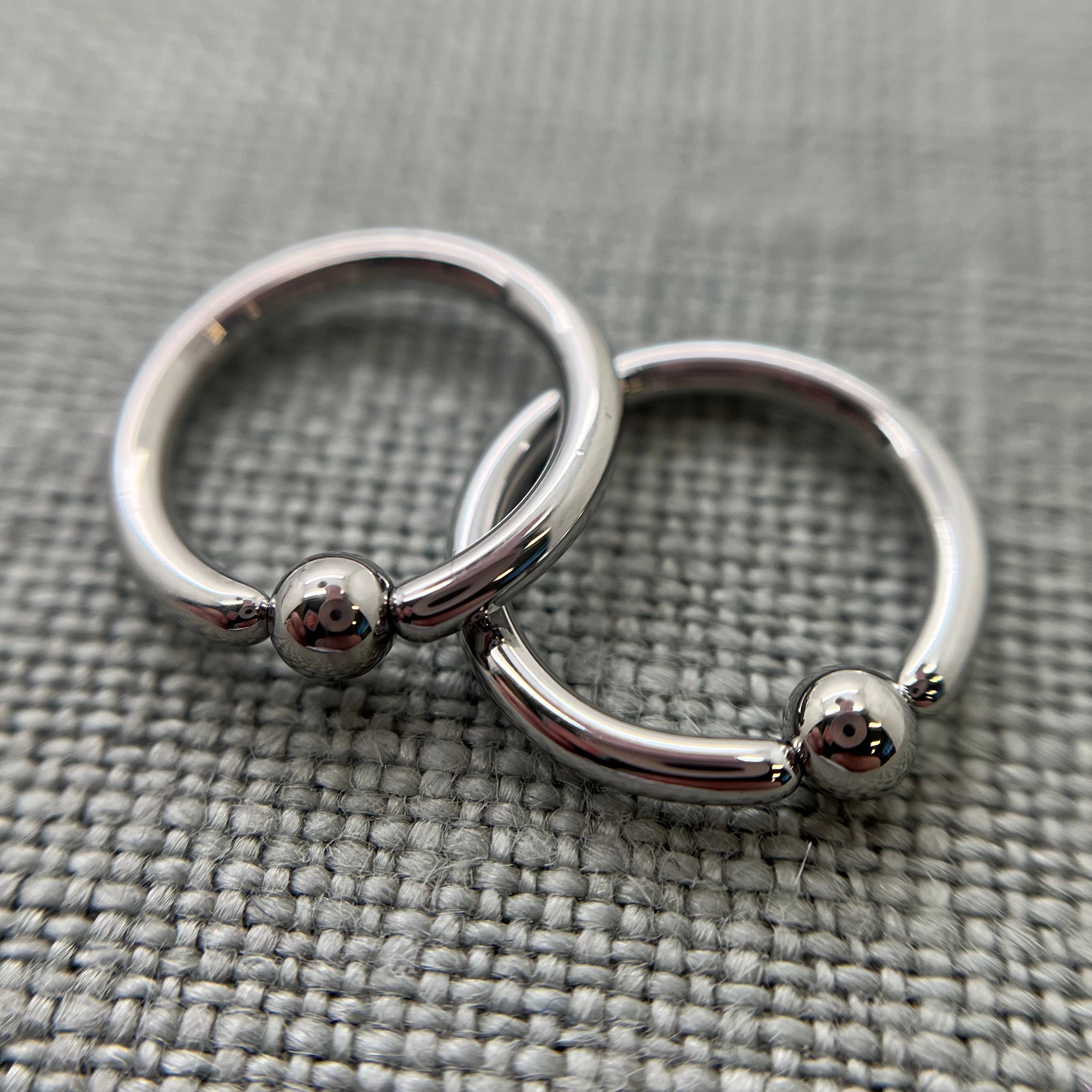Two polished stainless steel captive bead rings on grey fabric