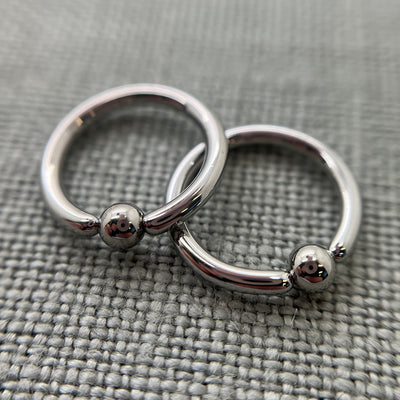 Two polished stainless steel captive bead rings on grey fabric
