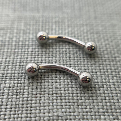 Two polished stainless steel curved barbells on grey fabric