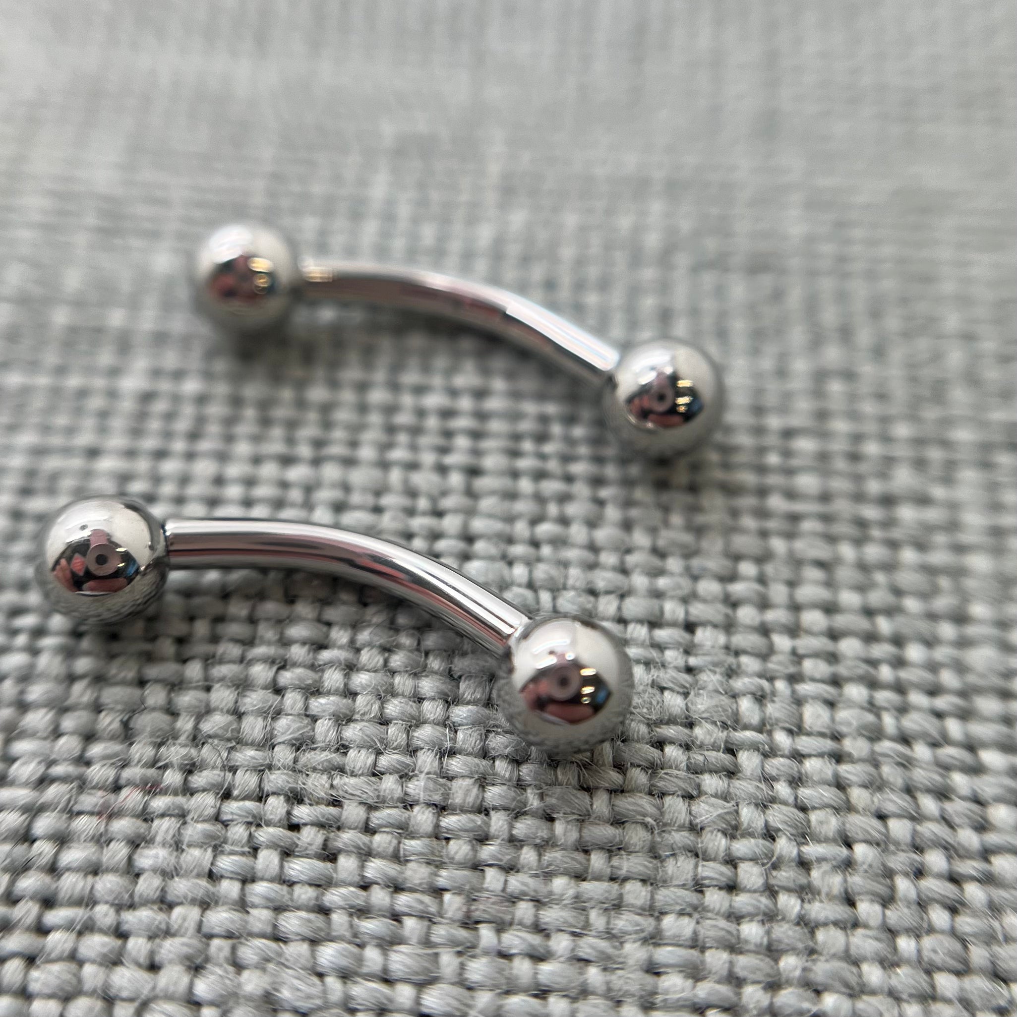 Two polished stainless steel curved barbells on grey fabric
