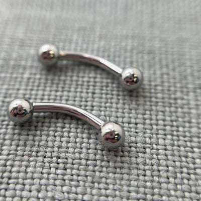 Two polished stainless steel curved barbells on grey fabric