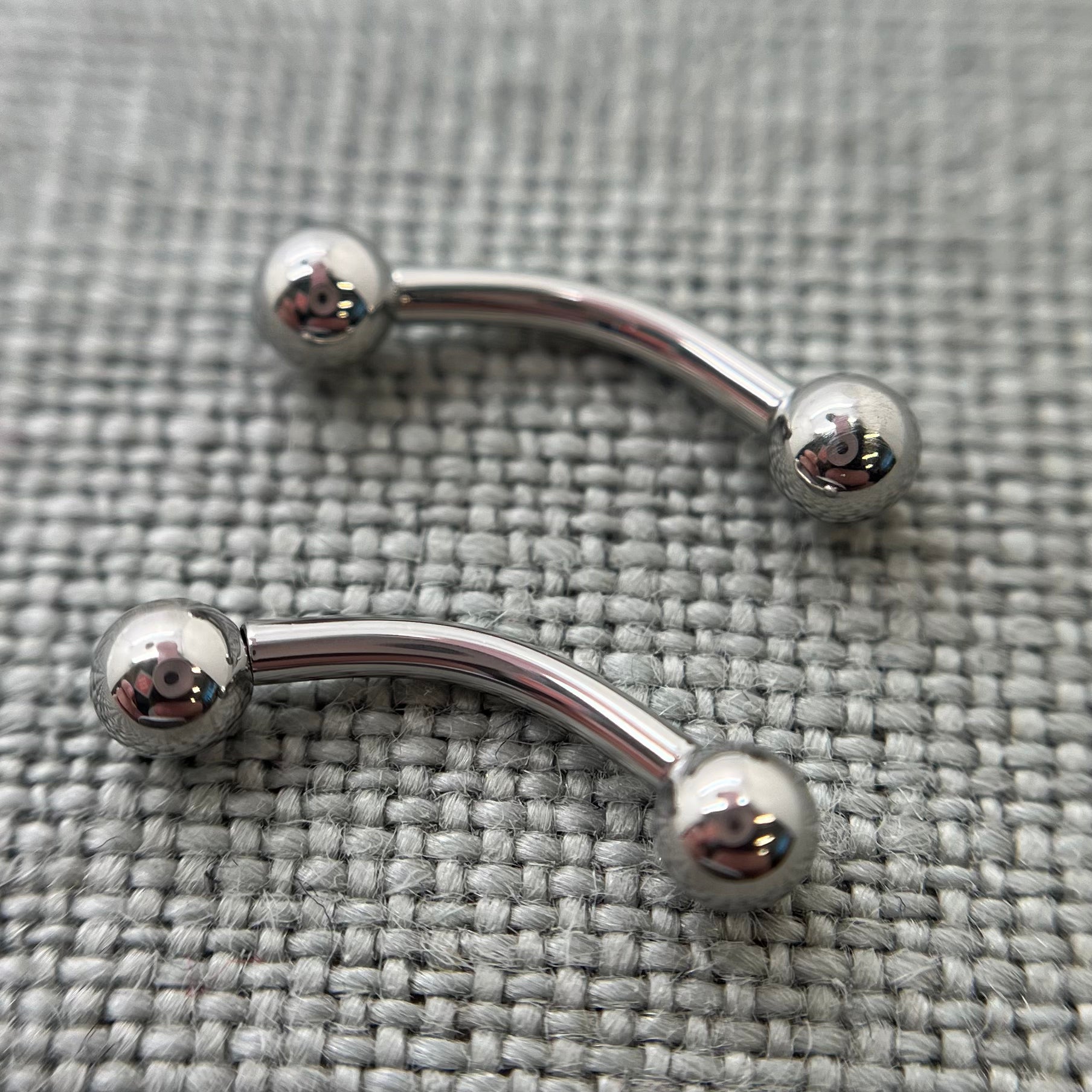Two polished stainless steel curved barbells on grey fabric