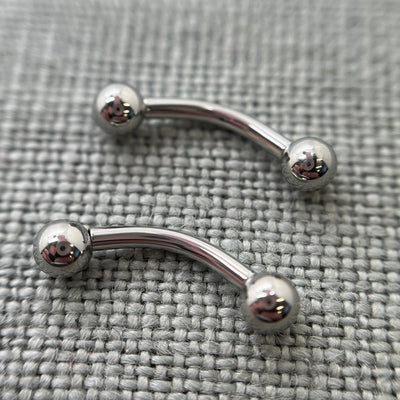 Two polished stainless steel curved barbells on grey fabric