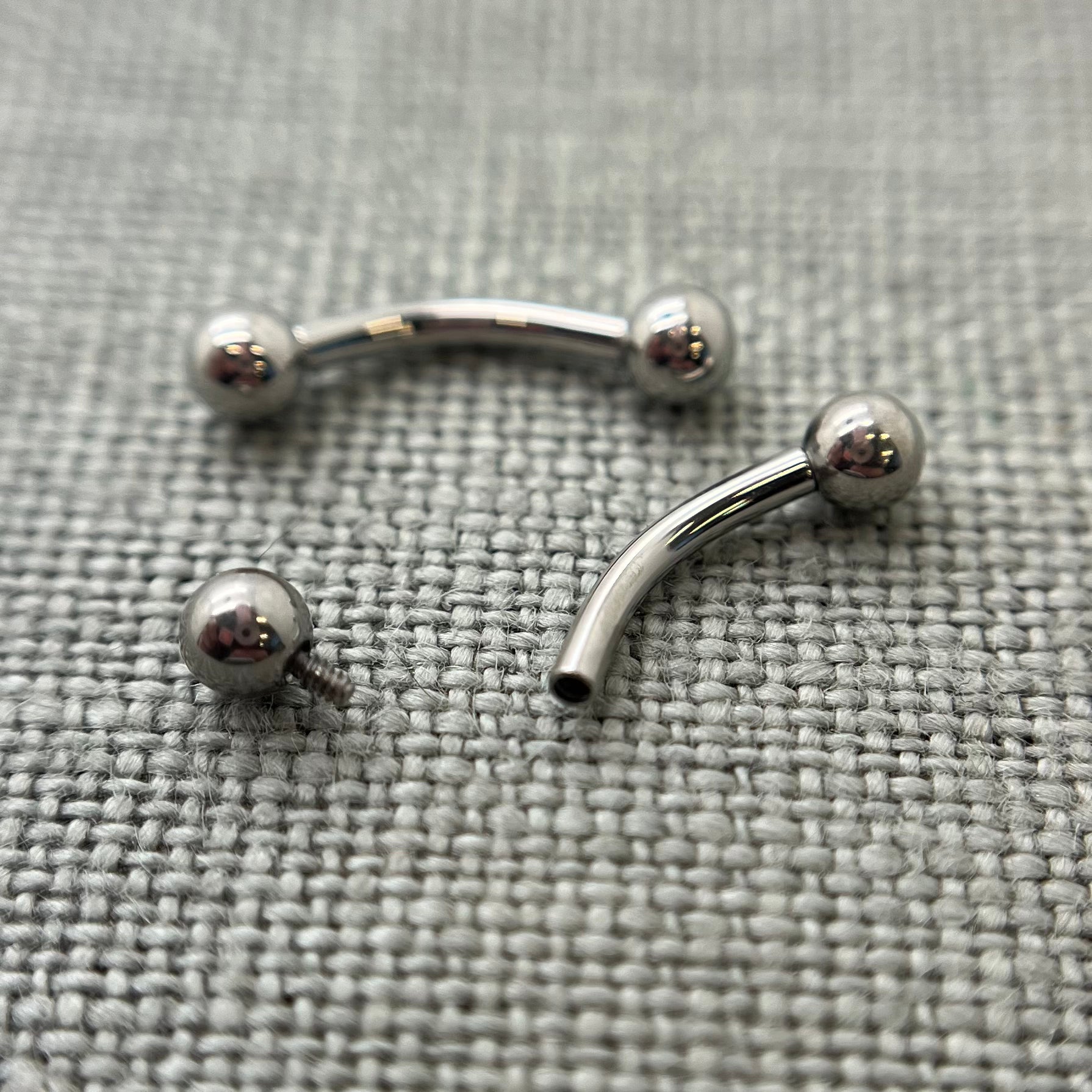 Two polished stainless steel curved barbells on grey fabric