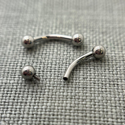 Two polished stainless steel curved barbells on grey fabric