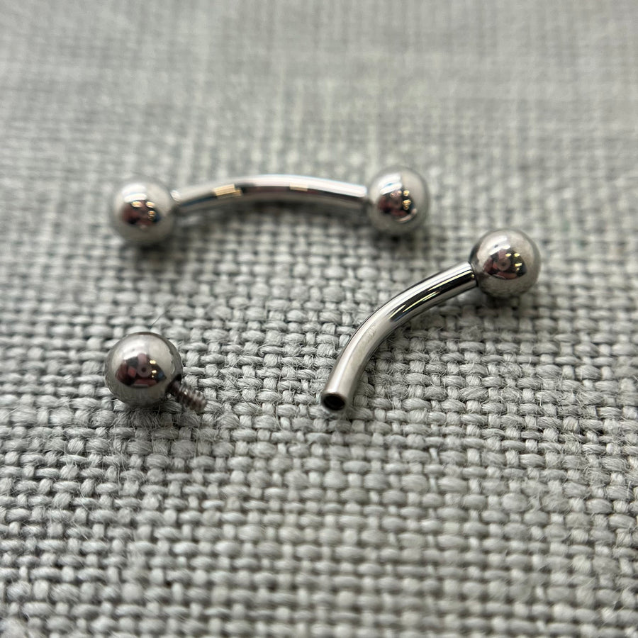 Two polished stainless steel curved barbells on grey fabric