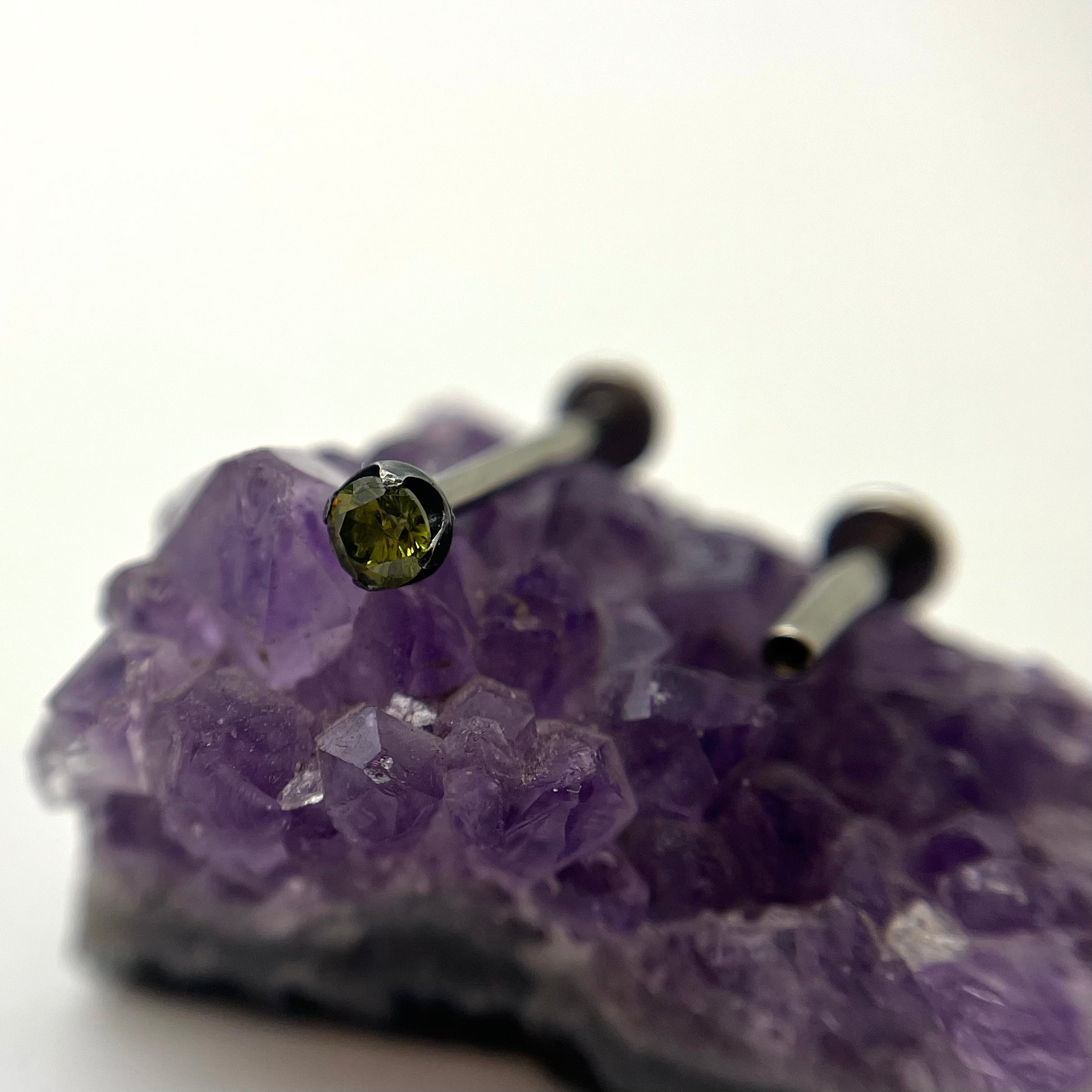 Green cubic zirconia in a black niobium setting on purple crystal