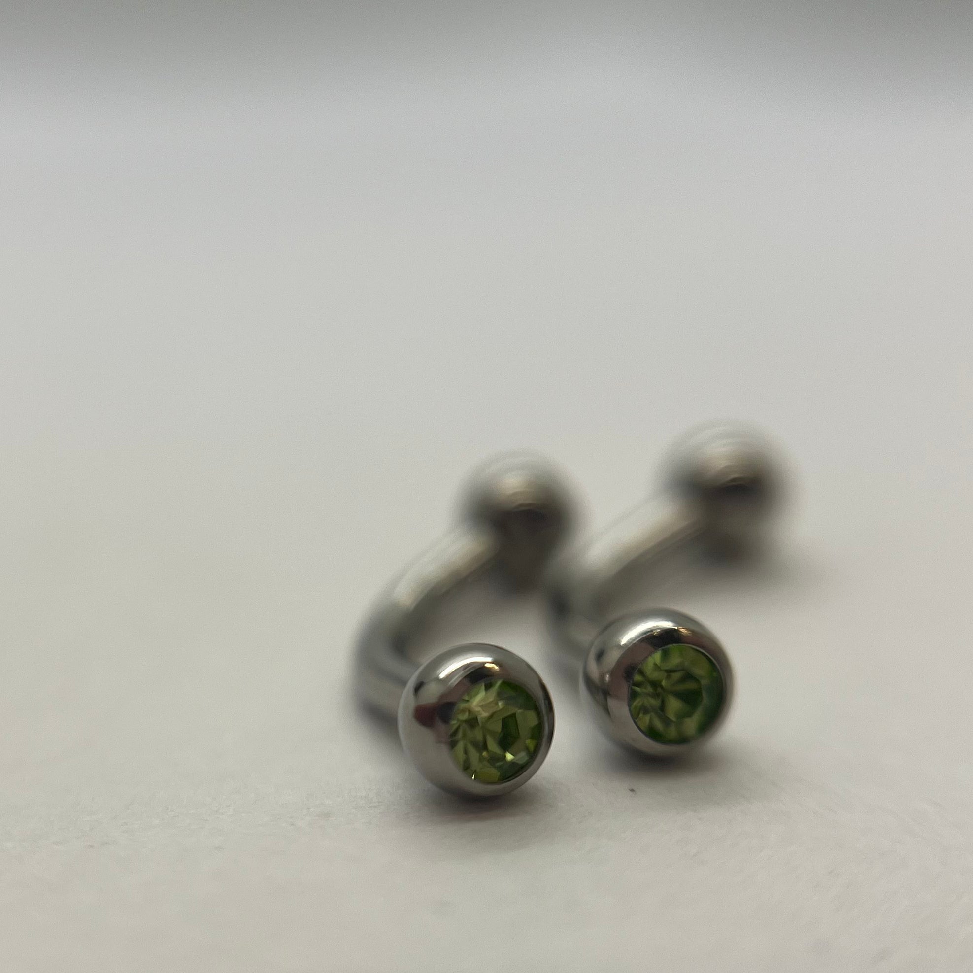 Stainless steel curved barbells with green cubic zirconia ends