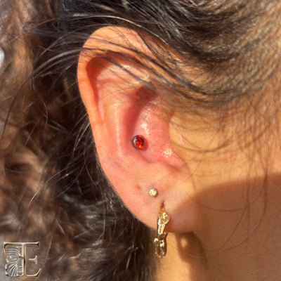 Red gemstone jewelry worn in a conch piercing above lobe jewelry