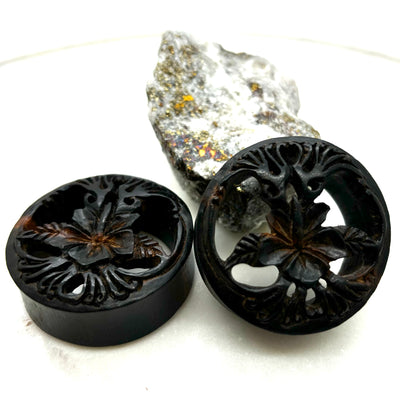 Carved dark wood double-flare plugs with an open tree design
