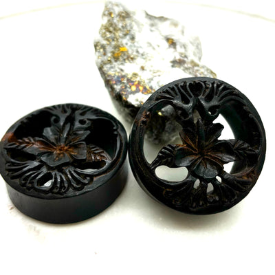 Carved dark wood double-flare plugs with an open tree design