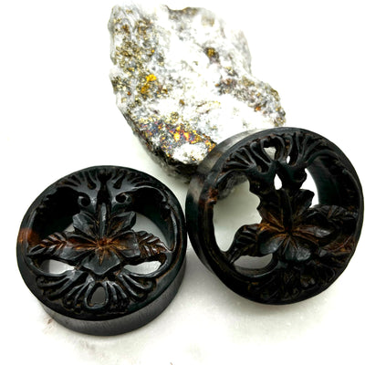 Carved dark wood double-flare plugs with an open tree design