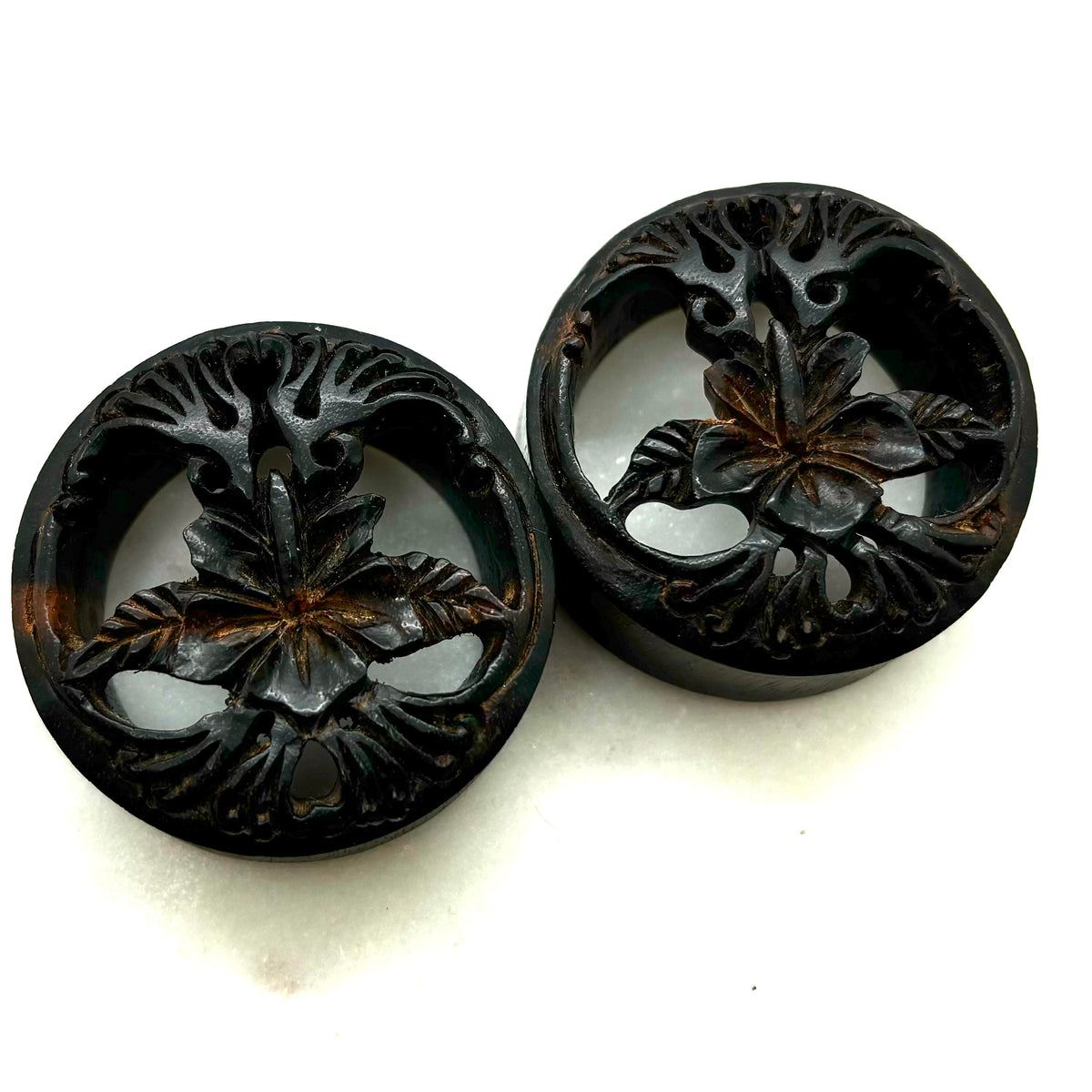 Carved dark wood double-flare plugs with an open tree design