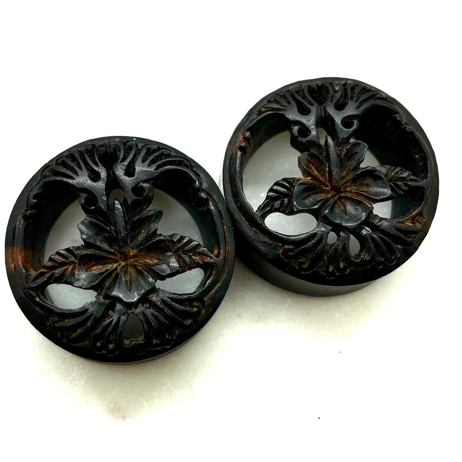 Carved dark wood double-flare plugs with an open tree design