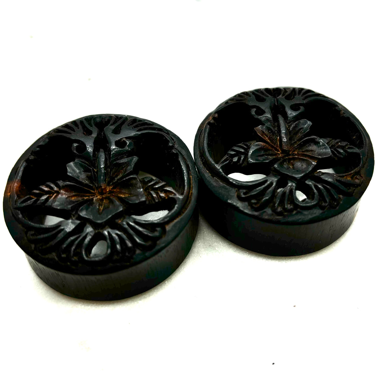 Carved dark wood double-flare plugs with an open tree design