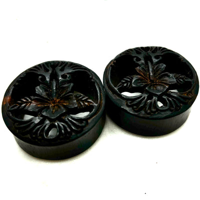 Carved dark wood double-flare plugs with an open tree design