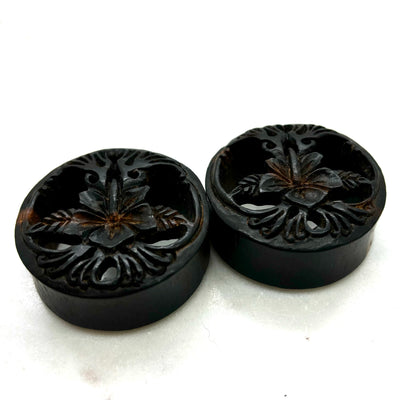 Carved dark wood double-flare plugs with an open tree design