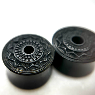Dark wood double-flare plugs with carved circular patterns and central openings